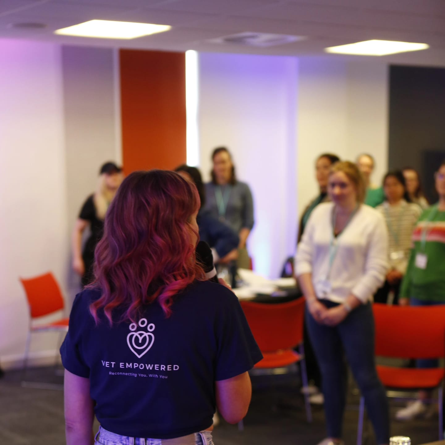 Claire Grigson, seen from behind in a Vet Empowered T-shirt, leading a workshop as a room of veterinary professionals stands facing her.
