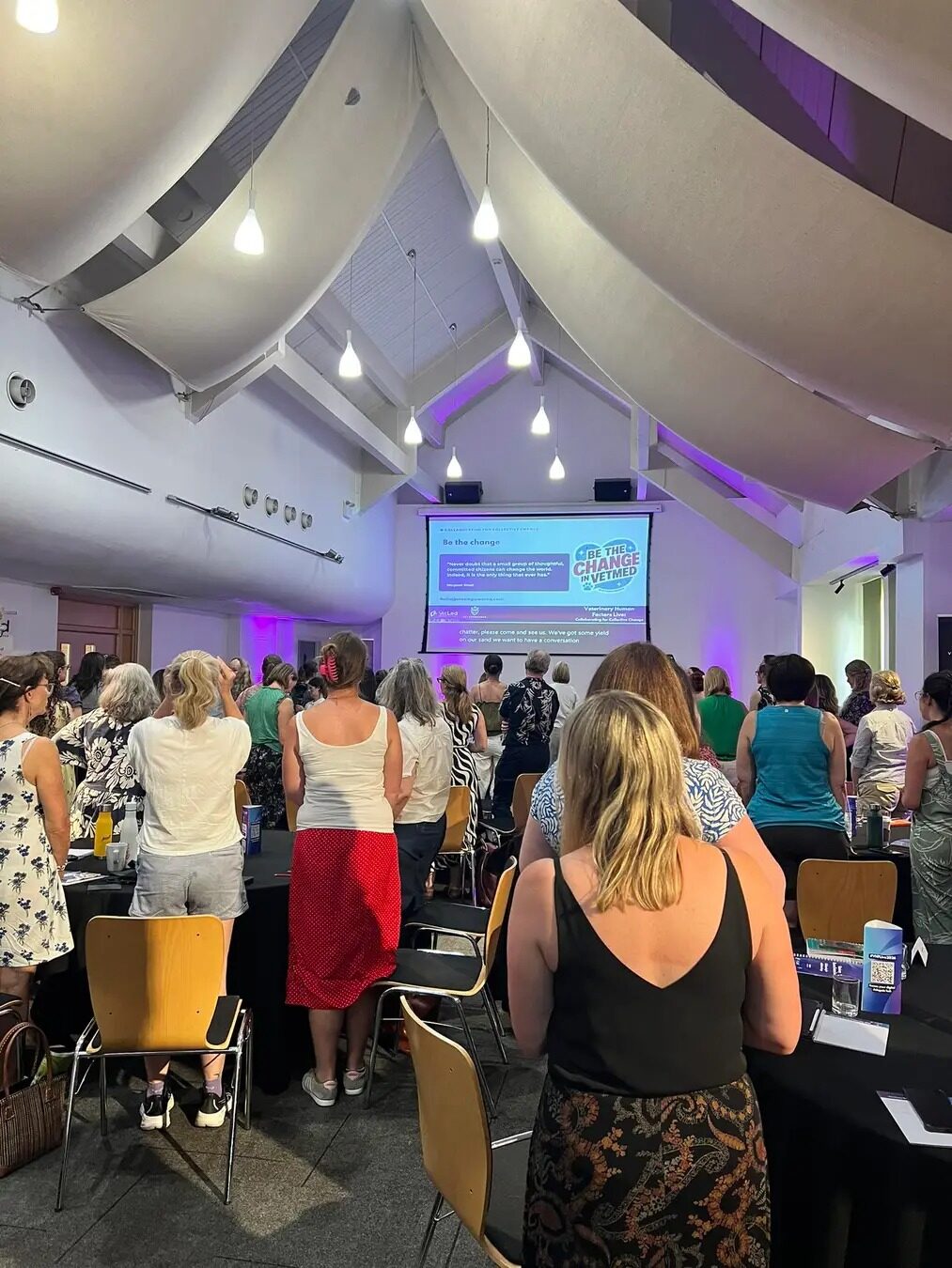 A full room of veterinary professionals at a Vet Empowered event, with a Be the change slide on screen